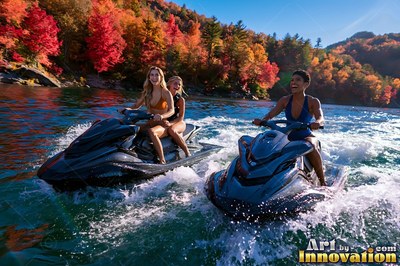 On a sunlit mountain lake, three smiling women ride jet skis past red fall trees