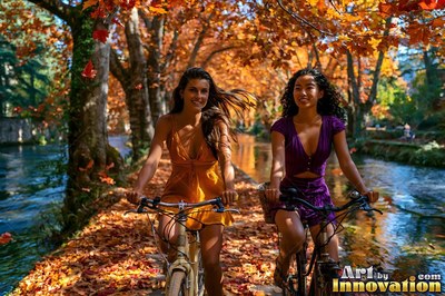 Along an autumn canal path, two smiling women travel on bicycles over fallen orange leaves
