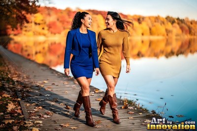 Walking side by side along a sunny lake, two women in dresses smile at each other