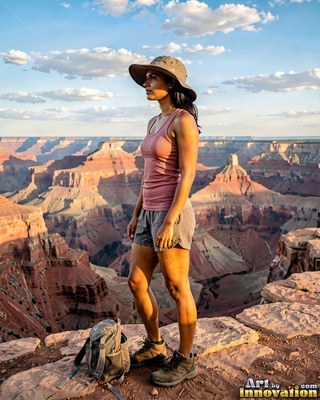 Standing in profile, a woman in a sun hat overlooks a red canyon rim