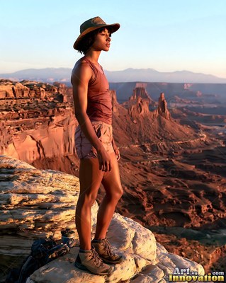 On a sunlit rim of the canyon, a woman in shorts and a hat stands looking into the distance
