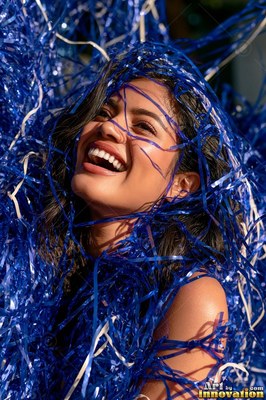 Smiling with bright white teeth in the sunlight, a woman is covered in shiny blue tinsel streamers
