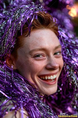 Laughing happily, a freckled redheaded woman is covered in purple tinsel garland