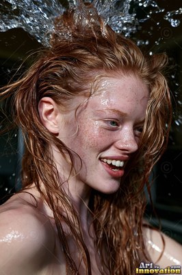 A smiling woman ends up splashed with water that shines brightly in her red hair