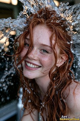 Smiling close-up of a red-haired woman outdoors as clear water splashes over her head