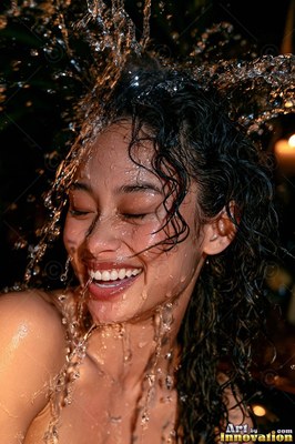 Smiling with eyes shut, a woman finds herself clear water splashed over her head and dark hair