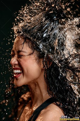 A chuckling woman squints as water splashes over her dark hair in bright side light