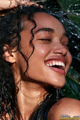 Wet curls frame the face of a woman laughing outdoors as water pours over her head