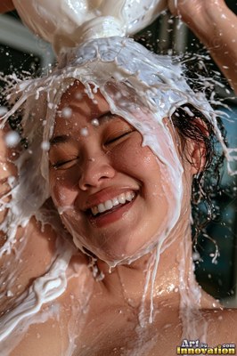 Smiling with eyes shut, a woman has plain white milk poured directly over her head