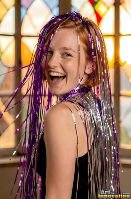 Freckles mark the smiling woman by a stained glass window as purple and silver streamers fall on her hair