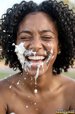 Outdoors, a smiling Black woman with curly hair gets splashed with thick white cream
