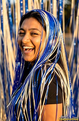 Laughing outdoors, a smiling woman wears blue and white party streamers over her dark hair
