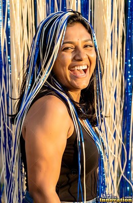 Under bright sunlight, a laughing woman has blue and white streamers draped in her hair