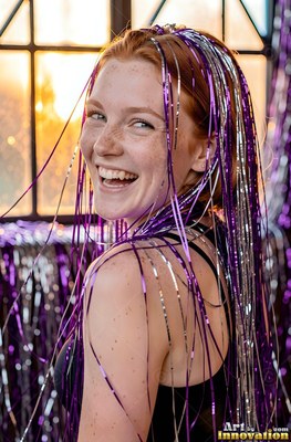 Smiling over her shoulder, a freckled woman wears shiny purple and silver tinsel in her hair