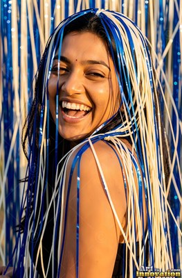 A cheerful woman giggles with blue and white party streamers draped over her head