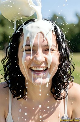 Dark wet curls frame a giggling woman in a sunny park as milk pours over her head