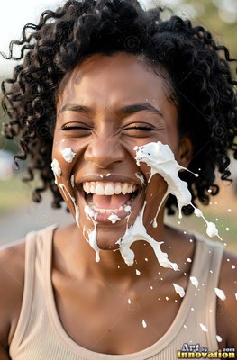 A laughing woman is splashed across the face with white cream outdoors in bright daylight