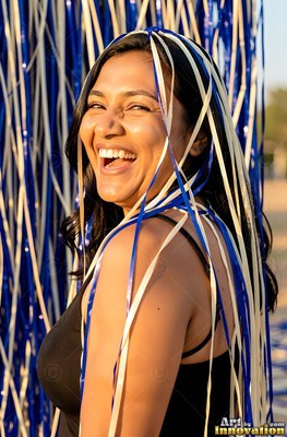 A woman chuckles as white and blue ribbons fall over her hair in warm golden sunlight