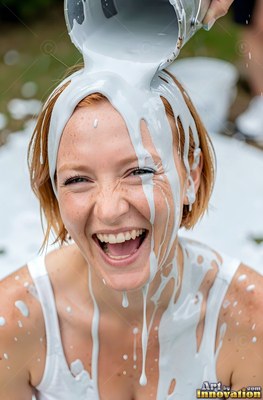 A smiling redhead woman in a white tank top gets thick paint poured on her head
