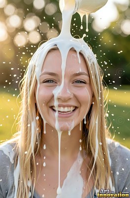 A smiling fair-haired woman getting milk poured over her head outdoors