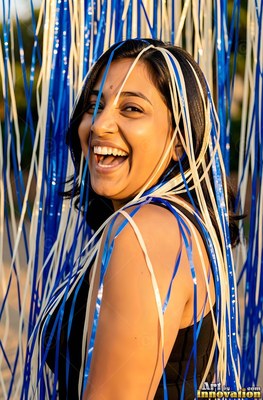 A bindi between her brows outdoors, a laughing woman stands under blue and white streamers