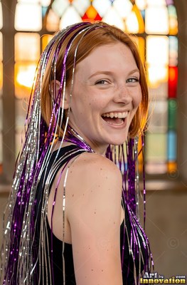 A grinning woman turns around with purple and silver tinsel draped over her hair
