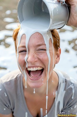 Freckles across her nose, a laughing woman gets white paint dumped on her outdoors in daylight