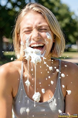 In a sunny park, a blond woman in a gray tank top laughs as whipped cream hits her face