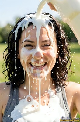 Facing forward outdoors, a smiling woman gets white milk poured over her head
