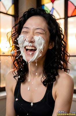A chuckling woman is hit in the face with plain white cream under soft window light