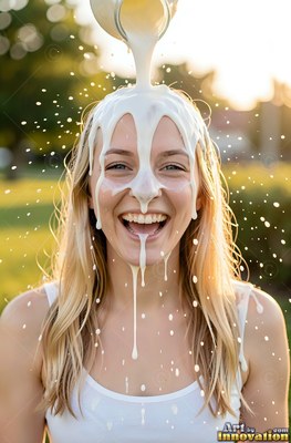 A smiling fair-haired woman is milk poured over her head in warm sunlight