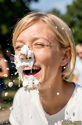 A blonde woman laughs as plain white cream hits her face in the bright outdoor sunlight