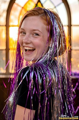 A smiling redhead woman in a black shirt has purple and silver tinsel draped on her head