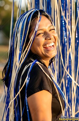 A woman with a smile laughs as blue and white streamers drape over her in warm sunlight