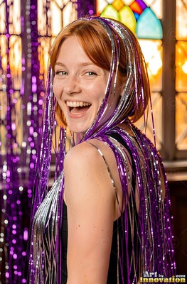Turned over her shoulder by a window, a woman with a smile wears purple tinsel