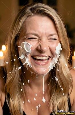 Head tilted forward indoors, a blonde woman laughs as thick white cream splashes her face