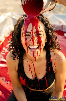 A woman chuckles as thick red paint pours over her head in the bright daylight