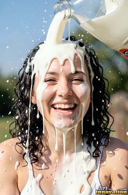Facing forward outdoors in the sun, a woman chuckles as milk covers her face