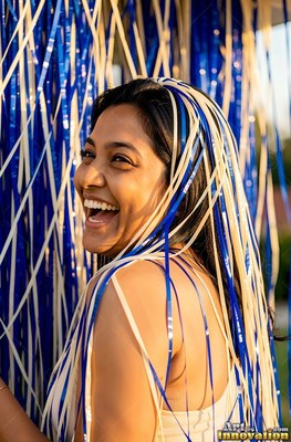 Outdoors in the sun, a smiling woman covered in blue and white party streamers