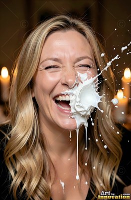 A woman with blonde hair in a black shirt laughs in a warm room as thick plain white cream splashes across her face