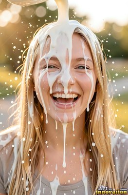 A blonde-haired woman bursts out laughing as thick splashing white milk pours over her head in warm sunlight