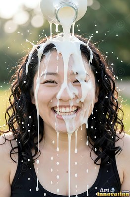 A smiling woman outdoors in a black tank top gets white milk poured over her face