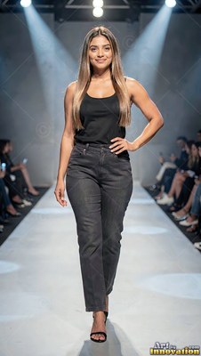 Dressed in a black tank top and dark jeans, a woman walks down a lit runway