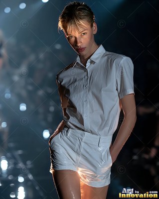 A woman walks the dark runway in a white shirt with warm light shining from below