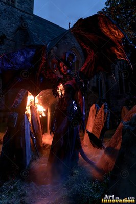 Standing by tombstones and fire, a horned demon woman spreads dark bat wings