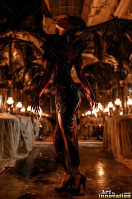 A horned woman in a black gown looks up in a dark candlelit hall