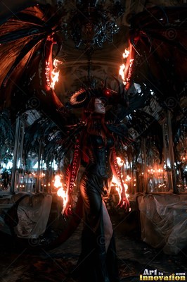 Standing with large black wings, a demon woman has fiery red symbols on her arms