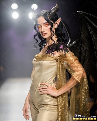 A horned woman in a gold dress walks a fashion runway with black wings