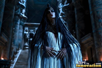 Standing in a dark stone hall, a fair-skinned woman dressed in a white gown and a wide gold collar