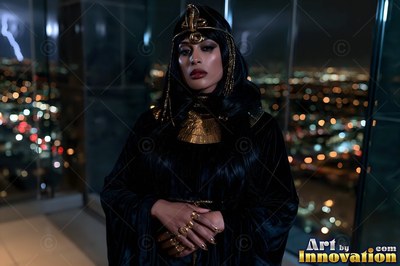 Facing forward on a high glass balcony, a woman stands in black and gold robes